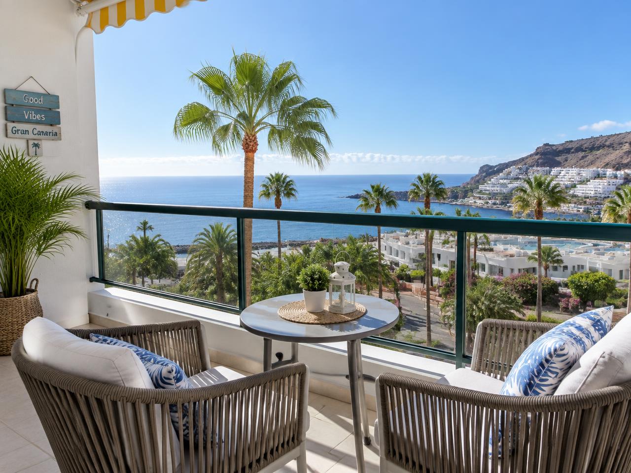 A holiday apartment balcony in Gran Canaria with chairs, palm trees and a sea view